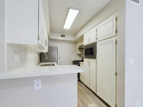 Apartments  for rent in Encino A modern kitchen featuring white cabinets, a stainless steel refrigerator, a built-in microwave, an electric stove, and a backsplash with white tiles. Overhead lighting illuminates the space. White Oak Apartments in Encino 5465 White Oak Avenue Encino, CA 91316  P: 866-471-5691 TTY: 711 F: 818-647-0393